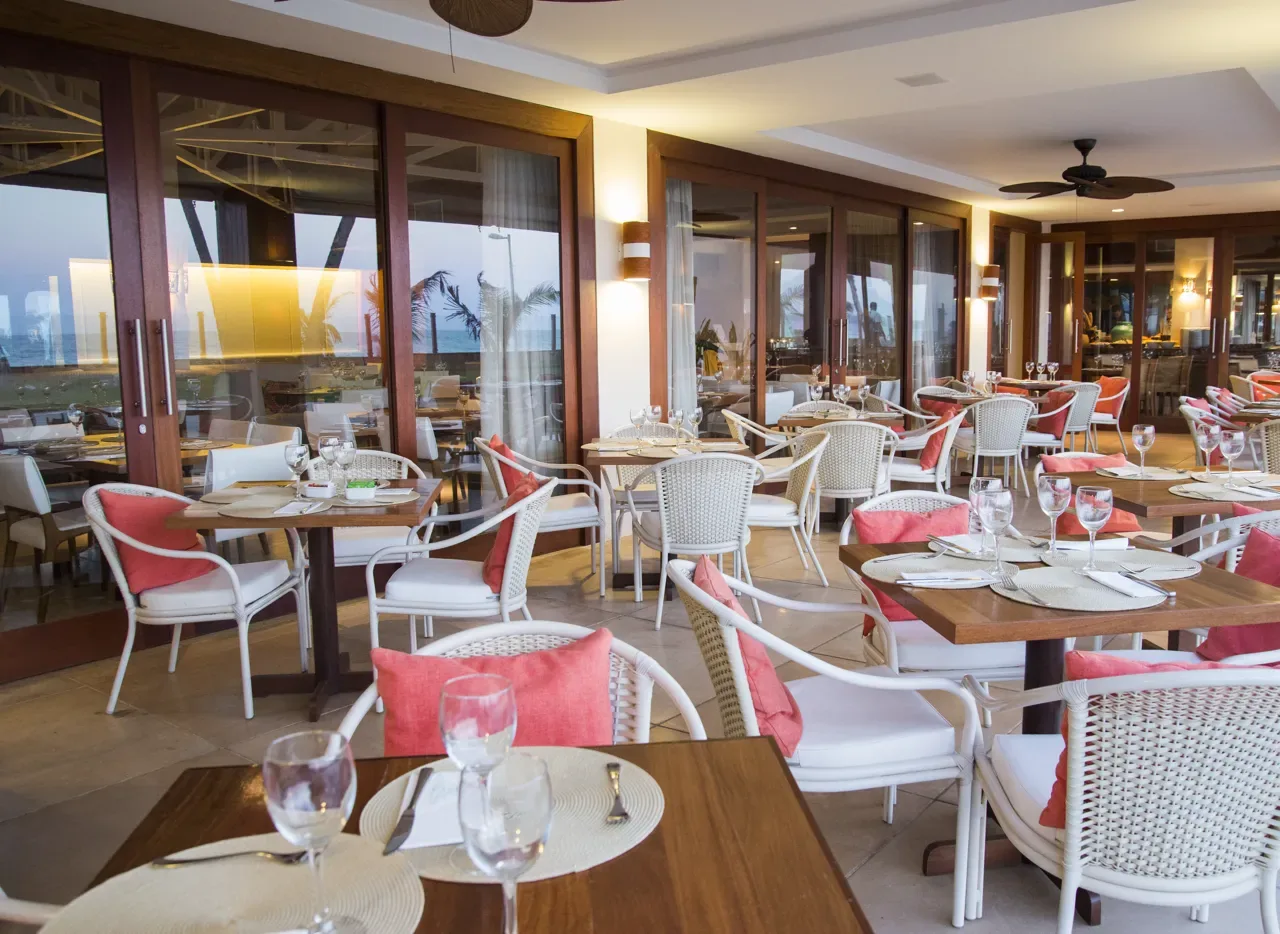 Salão do restaurante à beira-mar, com mesas postas e vista para a praia